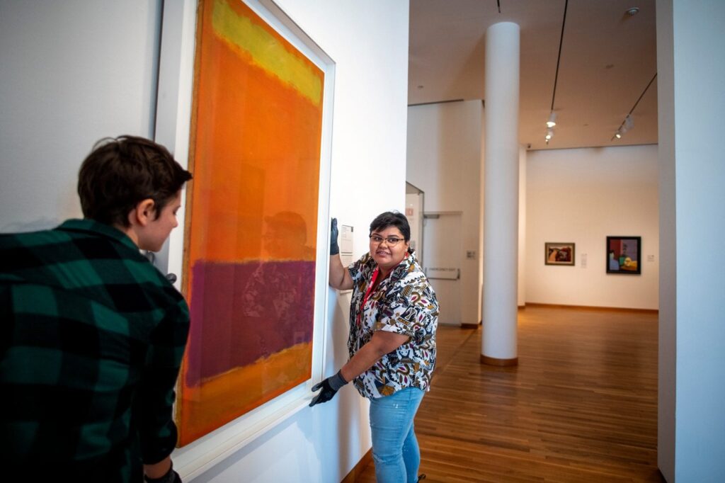 Two women hang a Rothko painting on a white wall