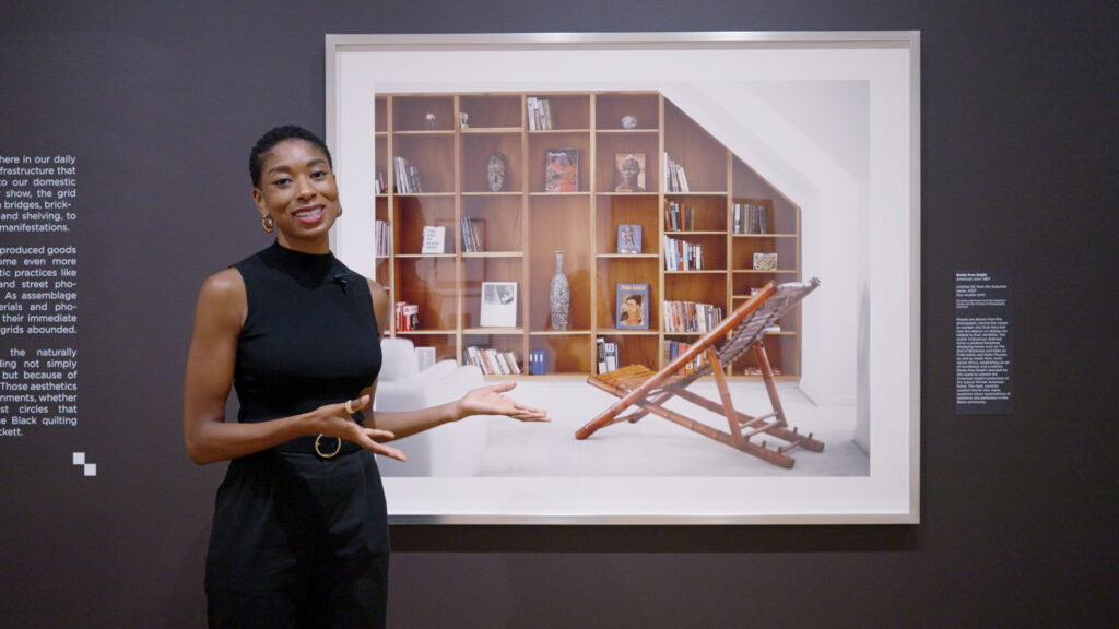 A woman smiles and gestures toward a large framed photograph