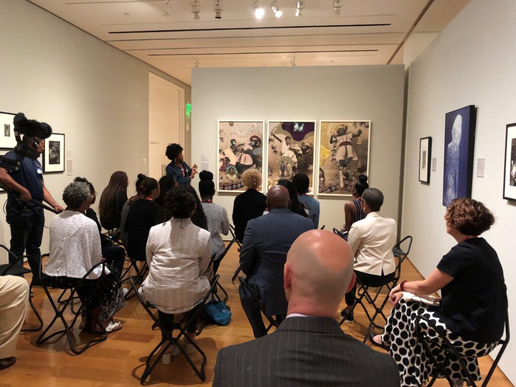 Group of people seated in chairs, viewed from behind as they look at art