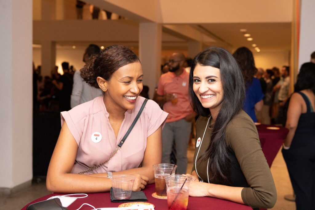 Two young women sit at a table with cocktails.