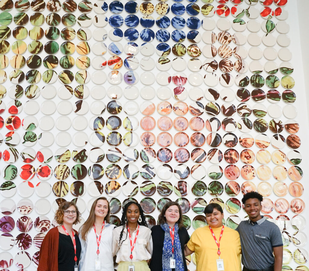 Six High Museum Summer Interns stand in front of Molly Hatch's plate wall sculpture