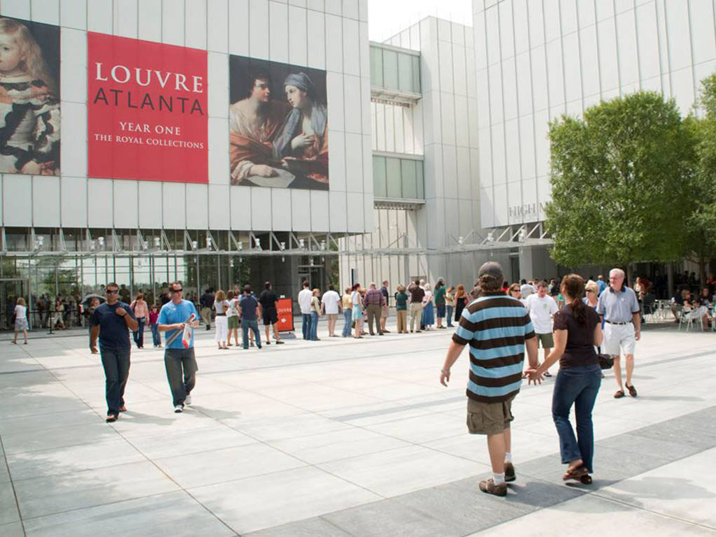People walking through the Sifly Piazza toward the High Museum's Anne Cox Chambers Wing. Banners announcing the Louvre Atlanta exhibition hang from the building.