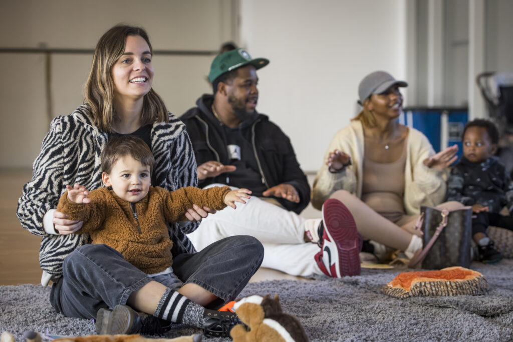A woman sits on the floor with a smiling toddler in her lap