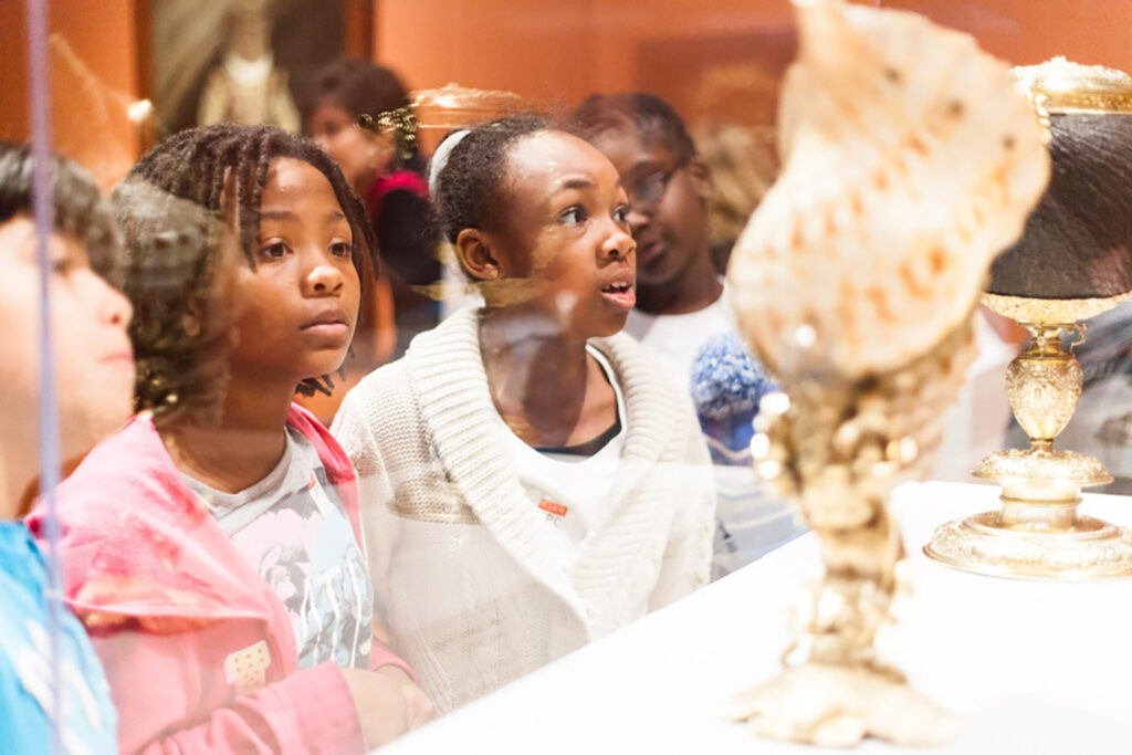 School children look through a glass case at objects in our decorative arts collection.