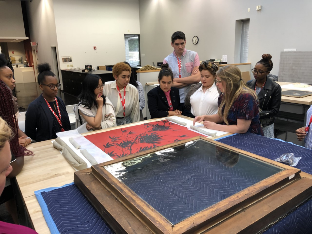 A group of students look at a printmaker's materials.